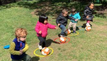 Toddlers with one foot on a soccer ball outside