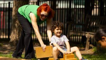 Teacher pushing preschooler on wooden car