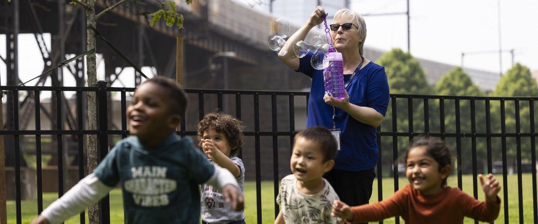 PCC Director blowing bubbles, with children running after bubbles