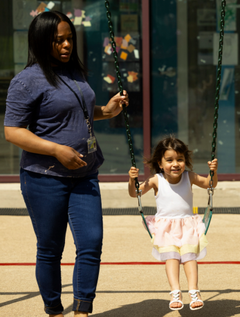 Preschool teacher pushing student on swing